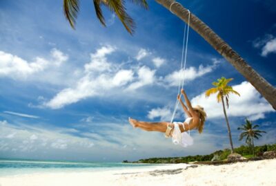 woman in cowboy hat swinging at a tropical beach